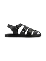 Sandalia tipo cangrejera de cuero graneado color negro, con diseño de tiras cruzadas decoradas con ojales metálicos. Cuenta con tira ajustable al tobillo con hebilla metálica y suela plana de PVC.