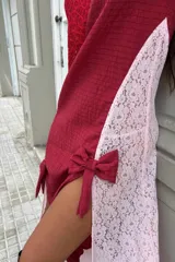 Vestido largo de encaje blanco con forro interior blanco, abertura lateral y detalle de lazo negro en la pierna. Se complementa con botas de cuero negras, chaqueta de cuero negra con flecos y gafas de sol negras.