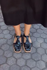 Sandalias de cuero negro con diseño de tiras entrecruzadas, hebilla dorada y suela plana.