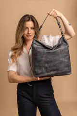 Cartera tipo bandolera de gran tamaño, confeccionada en cuero sintético con acabado desgastado. Cuenta con una asa corta fija, una correa larga regulable y extraíble, y una placa metálica con la marca en la parte frontal.