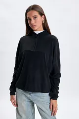 Buzo de polar negro con cuello alto y cierre frontal parcial. Presenta un diseño de corte holgado con mangas largas y costuras horizontales en el pecho.