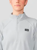 Polar gris de mujer Mountain Hardwear modelo Microchill 1/4 Zip, con cuello alto, cierre frontal parcial de un cuarto y mangas raglán. Presenta un parche con el logotipo de la marca en el pecho.