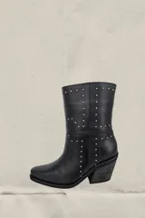 Bota corta de cuero vacuno color negro, con diseño de caña media y taco cuadrado. Presenta detalles de tachas metálicas plateadas distribuidas por toda la superficie y puntera redondeada.