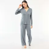 Pijama de dos piezas compuesto por una camisa de manga larga con botones frontales, cuello solapa y bolsillo en el pecho, y un pantalón de corte recto y holgado. Ambas prendas presentan un diseño liso en color gris con detalles de ribetes en contraste.
