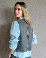 Chaleco de corte recto y largo a la cintura, confeccionado en denim con estampado de rayas verticales en tonos azul y blanco. Presenta cuello redondo y costuras visibles que definen su estructura.