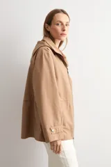 Trench color camel con capucha desmontable, cierre frontal con cremallera, bolsillos laterales y mangas largas con ajuste en puños.