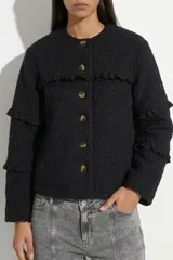 Campera de tela bouclé color negro, con diseño de cuello redondo y cierre frontal mediante botones. Presenta detalles de volados en tela agamuzada en el pecho y en las mangas.