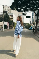 Camisa de rayas verticales azules y celestes, con cuello solapa, escote en V, cierre frontal con botones y mangas largas abullonadas con puños ajustados.