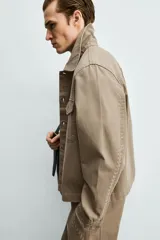 Sobrecamisa de corte boxy fit confeccionada en algodón con estructura canvas y efecto lavado. Presenta cuello solapa, cierre frontal con botones, mangas largas con puños abotonados y bolsillos de plastrón con solapa en el pecho. Incluye detalles bordados a tono en las mangas.