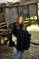 Poncho de lana merino color negro, con cuello alto, diseño amplio y terminaciones con flecos en todo el borde.