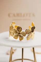 Pulsera dorada rígida con diseño de flores caladas en acero quirúrgico con baño de oro de 18k.