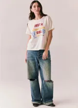 Remera blanca de manga corta y cuello redondo, con estampado frontal de estilo retro con la inscripción "Just a Small Town Girl Journey" acompañada de gráficos florales en tonos rojo, amarillo y azul.