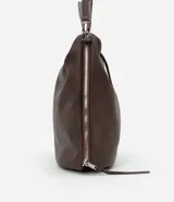 Bolso hobo grande desestructurado color marrón oscuro, con correa de mano y correa larga desmontable. Presenta cierres laterales ajustables con tiradores y cierre superior.