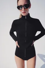 Chaqueta de punto negra con cuello subido y cierre frontal con cremallera, de manga larga y diseño ajustado.