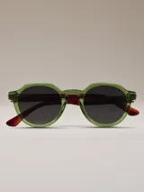 Lentes de sol con armazón de acetato verde translúcido, forma redonda con lados ligeramente facetados. Las patillas son de color marrón carey.