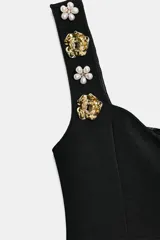 Top negro de tejido elástico, corte peplum, escote corazón y tirantes anchos decorados con aplicaciones de joyas doradas en forma de flor.