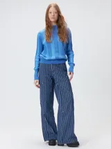 Sweater de punto con diseño de rayas verticales en tonos negro y gris oscuro. Presenta cuello alto tipo polera, mangas largas con puños ajustados y ruedo elástico. Incluye un pequeño bordado en color rojo en el pecho.