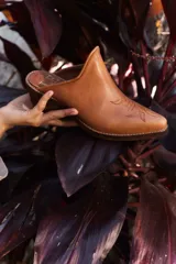 Mule de cuero color suela con diseño de punta fina y bordado decorativo en el empeine. Presenta un taco bajo de madera y una silueta abierta en el talón.