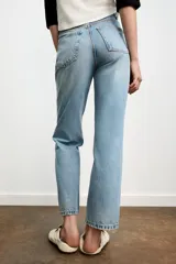 Jeans de mujer, tiro alto, color azul medio con efecto desgastado (lavado claro en muslos y oscuro en bordes). Corte recto y ancho (mom fit) con cinco bolsillos y cierre frontal de botón y cremallera.