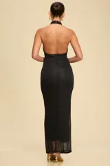 Vestido largo de tejido metallic knit color negro, con cuello halter y espalda descubierta. Presenta un diseño ajustado al cuerpo con detalles drapeados en la zona de la cadera.