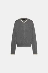 Chaqueta de punto gris oscuro, de manga larga y corte recto, con cuello redondo y puños terminados en puntilla de color claro a contraste.