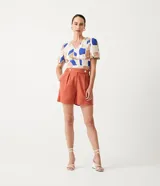 Short de lino color terracota, de tiro alto, con pliegues frontales y dos botones decorativos en la cintura.