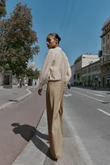 Pantalón de tiro medio con pernera ancha, confeccionado con pinzas delanteras y bolsillos laterales. Presenta un cierre frontal con cremallera y un botón decorativo dorado con relieve.