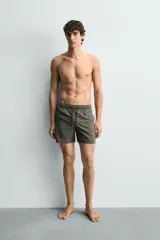 Bañador de hombre de largo medio, color celeste claro con rayas blancas horizontales. Presenta cintura elástica ajustable con cordón, bolsillos frontales y bolsillos traseros de plastrón. Incluye forro interior.