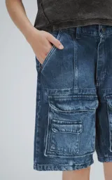 Bermuda de denim azul oscuro con lavado y efecto desgaste, corte oversize y estilo cargo con múltiples bolsillos con tapa en las piernas.