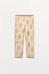 Pantalón tipo legging de encaje color dorado/beige, con patrón floral y acabado semitransparente. Presenta cintura y puños elásticos.