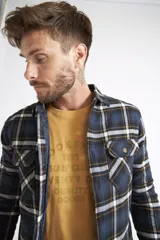 Sobrecamisa de viyela para hombre con estampado de cuadros en rojo y negro. Presenta cierre frontal con botones, bolsillos en el pecho con solapa y botón, y un interior capitoneado para mayor abrigo. Cuenta con un logo en grifa de cuero.