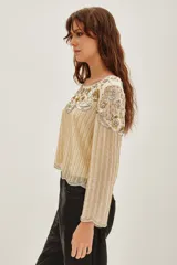 Camisa de manga larga en color crema, con diseño bordado en hilos dorados y plateados que forman líneas verticales y detalles florales en el pecho. Presenta un estilo elegante y sofisticado con aplicaciones brillantes.