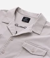 Camisa boxy color crema de algodón texturizado, con cuello inglés, mangas cortas, bolsillos delanteros y lettering bordado.