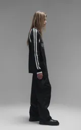 Sweater de punto negro con cuello redondo, mangas largas con franjas laterales blancas y puños en punto rib. Presenta un diseño gráfico bordado en el pecho con la inscripción 'RAVERS' y detalles en blanco.