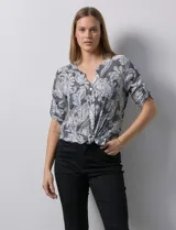 Blusa de gasa estampada en tonos grises y blancos, marca Ruby Rd. Tiene cuello a la base con escote en V y abertura con botones. Cuenta con bolsillos delanteros, mangas 3/4 regulables con presilla y botón, y terminación de ruedo con nudo.