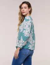 Blusa de gasa texturizada color verde con estampado floral blanco, cuello mao con escote en V y botones frontales. Cuenta con mangas 3/4 abullonadas y detalles de puntilla calada en el pecho.