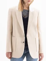 Blazer de tweed color beige, de corte recto y largo medio, con solapa clásica en contraste color blanco, dos bolsillos frontales con parche y cierre de dos botones plateados.