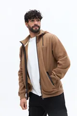 Campera de felpa color camel con cierre frontal, capucha ajustable con cordones negros y bolsillos laterales con cierre negro. Presenta un estampado pequeño en el pecho con texto en color oscuro.