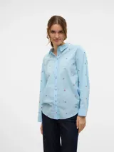 Camisa de manga larga color celeste, con cuello clásico y cierre frontal de botones. Presenta un estampado de cerezas rojas y puños abotonados. Confeccionada en tejido plano de algodón orgánico.