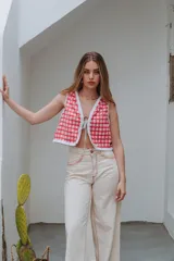 Chaleco corto de paño de lana tejido, con diseño a cuadros en tonos rojo y blanco, ribetes blancos con flecos y cierre frontal mediante lazos de cuero.