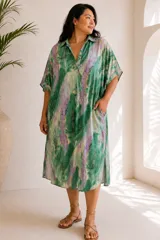 Túnica midi de seda con estampado estilo tie-dye en tonos verde, lila y blanco. Cuenta con cuello camisero, escote en V profundo, mangas cortas amplias, bolsillos laterales y calce oversize.