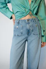 Jeans de tiro alto con corte wide leg y pernera ancha. Presenta bolsillos de plastrón en el delantero y cierre frontal con cremallera y botón.