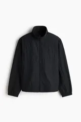 Campera rompevientos de nylon color negro, repelente al agua, con cuello elevado, cierre frontal y bolsillos laterales. Cuenta con forro de malla y puños con elástico.
