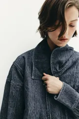 Cazadora corta de denim con efecto lavado, cuello solapa amplio, manga larga y cierre frontal cruzado con botones a presión. Presenta bolsillos laterales de vivo.