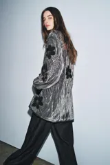 Kimono de terciopelo gris con acabado texturizado, cuello redondo y manga larga. Presenta bordados florales en hilo negro y metalizado, bolsillos delanteros y cierre frontal.