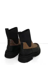 Botín de caña media con diseño bicolor, combinando cuero texturizado en color suela en la parte frontal y cuero liso negro en la puntera y talón. Presenta una caña de neopreno elastizado en color negro y suela de goma track con plataforma.