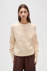 Sweater de tejido de punto en color crema con diseño de líneas en zigzag bordadas en hilo rosado. Presenta cuello redondo a la base, mangas largas con costura raglán y corte holgado.