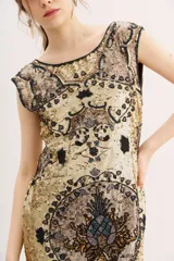 Vestido corto de lentejuelas doradas con diseño estampado de corazones y motivos ornamentales en tonos oscuros. Presenta un corte recto y sin mangas.