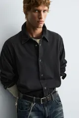 Camisa de corte relajado confeccionada en algodón con efecto lavado. Presenta cuello solapa, manga larga y cierre frontal con botones a presión metálicos.