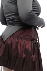 Minifalda negra de tafeta con cintura alta elastizada, diseño con volado y lazos laterales ajustables.